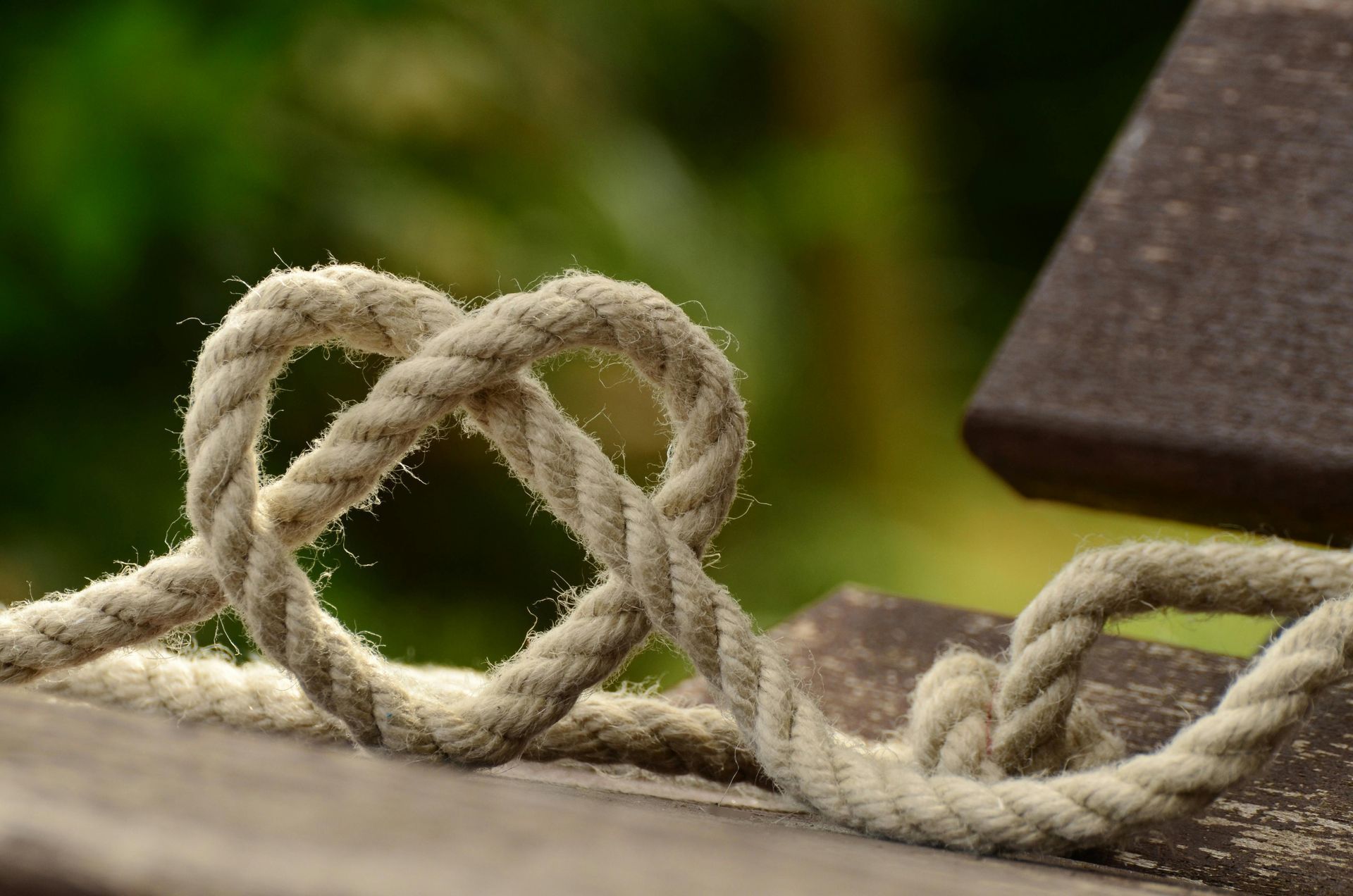 Heart-shaped knot made from thick rope on a wooden bench, with blurred green background.