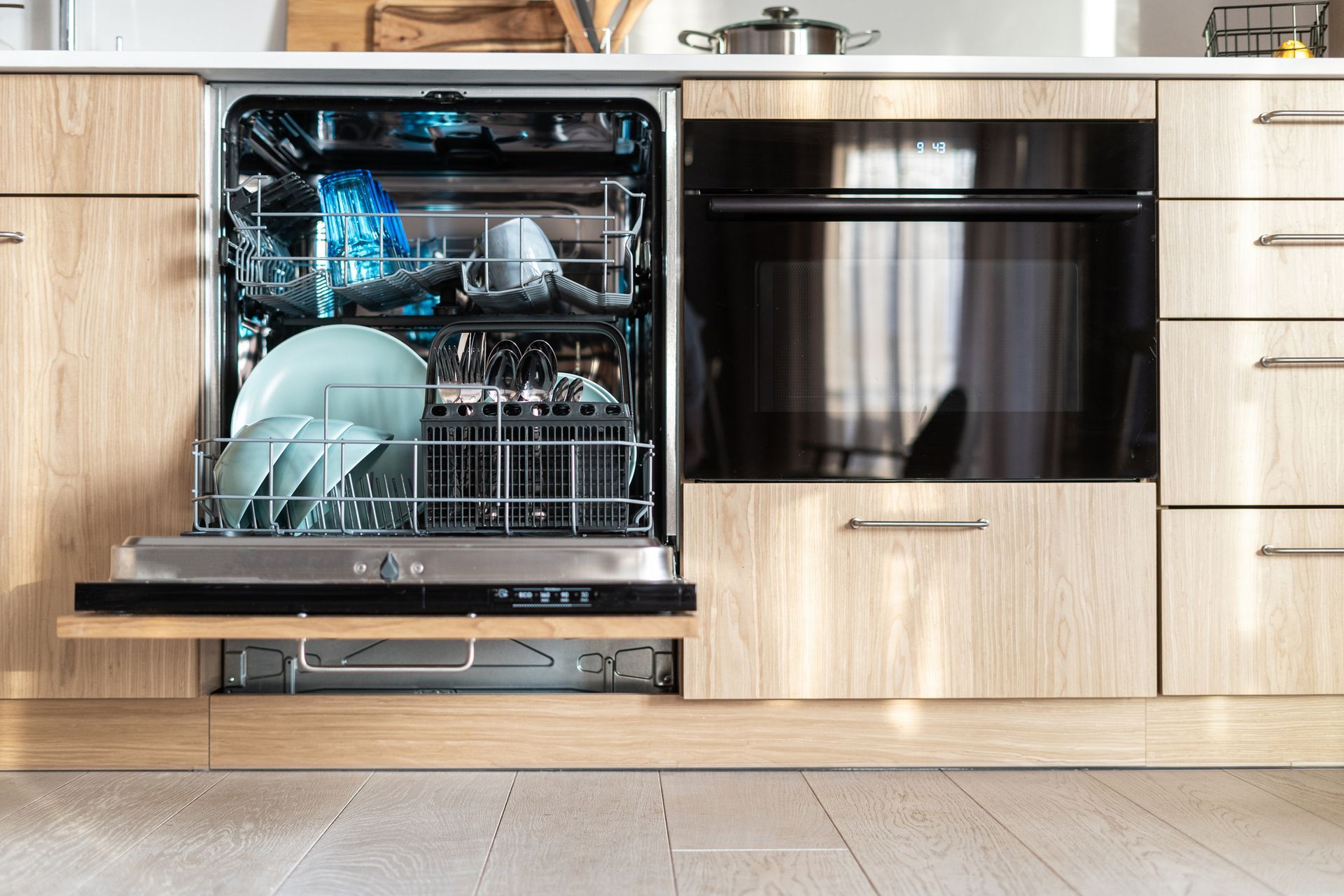 Dishwasher open with dishes inside, next to an oven; both are built into wood cabinets.