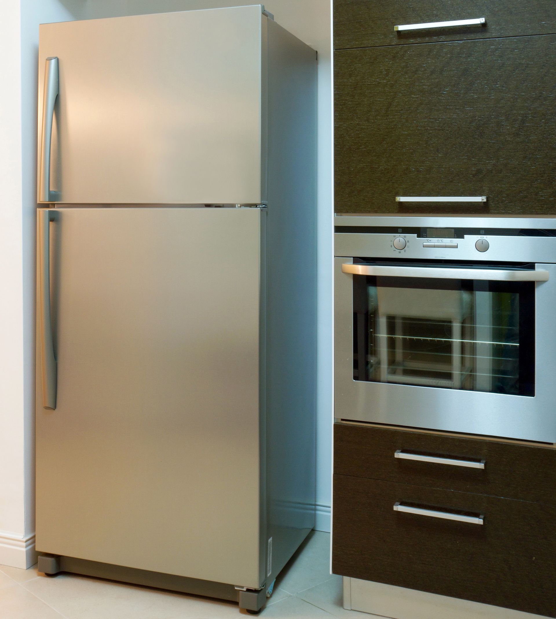 Stainless steel refrigerator beside a built-in oven and brown cabinets in a kitchen.