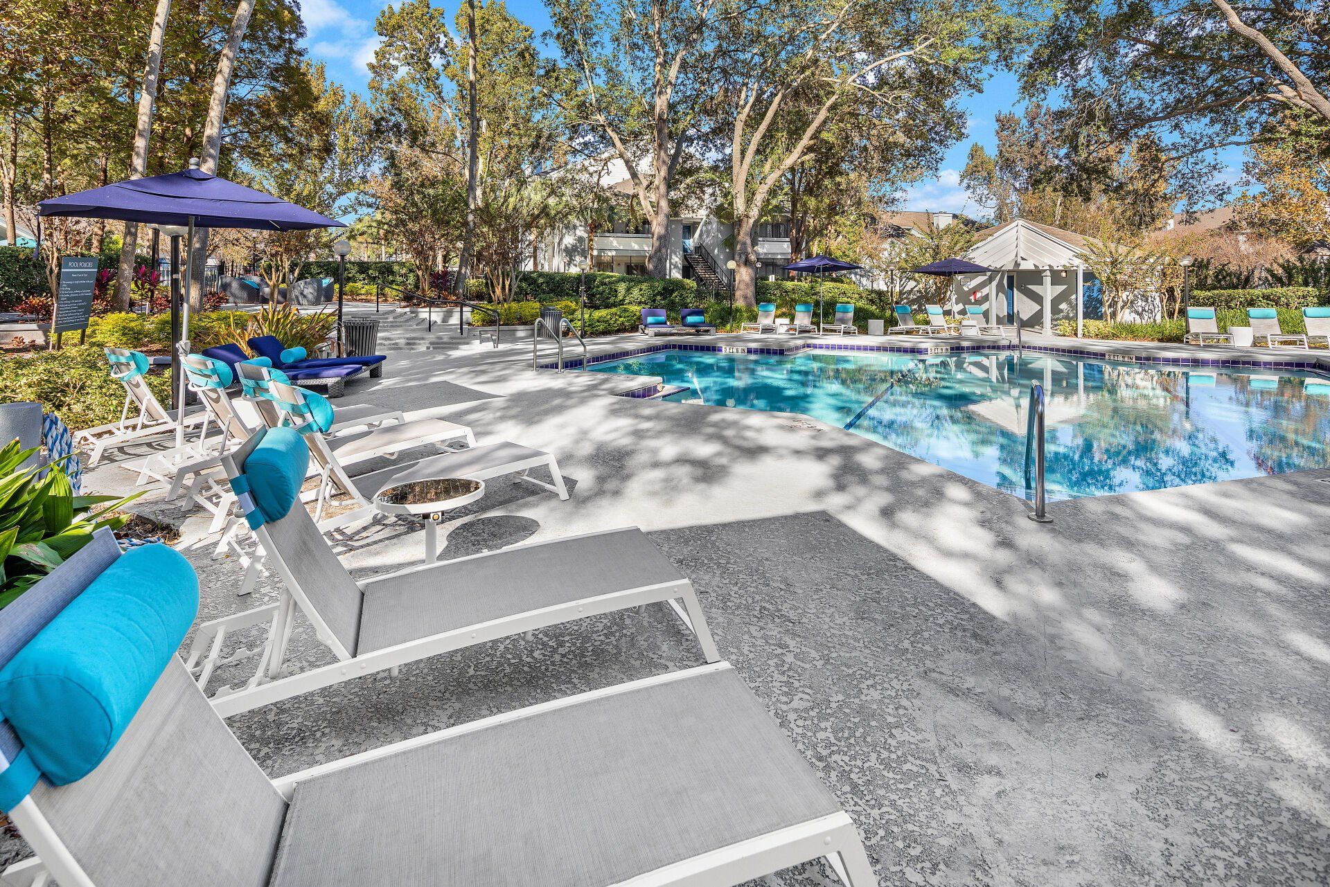 There are a lot of chairs and umbrellas around the pool.