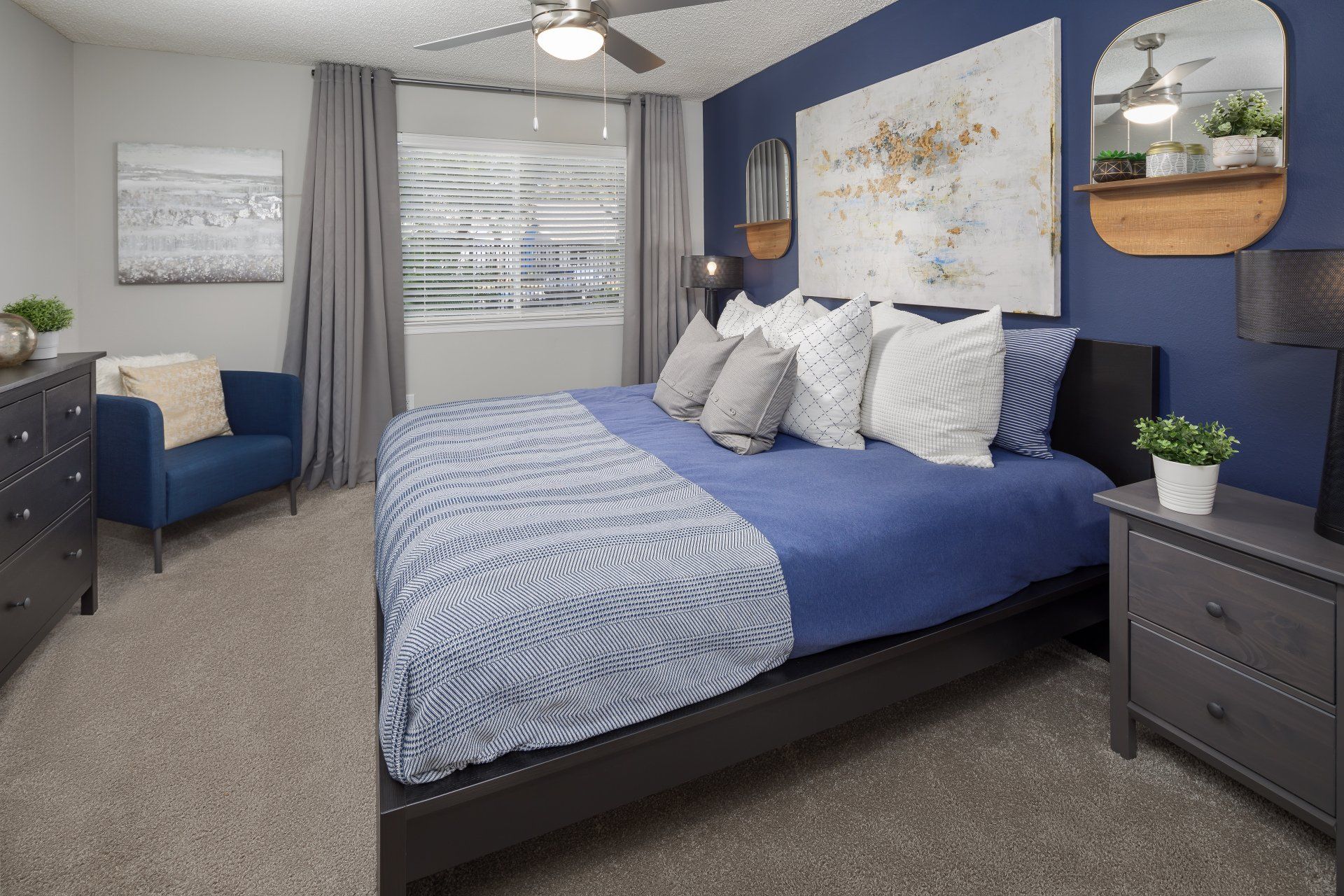1801 Metrowest apartment bedroom with oversized window, ceiling fan, bed, wall art and sofa.