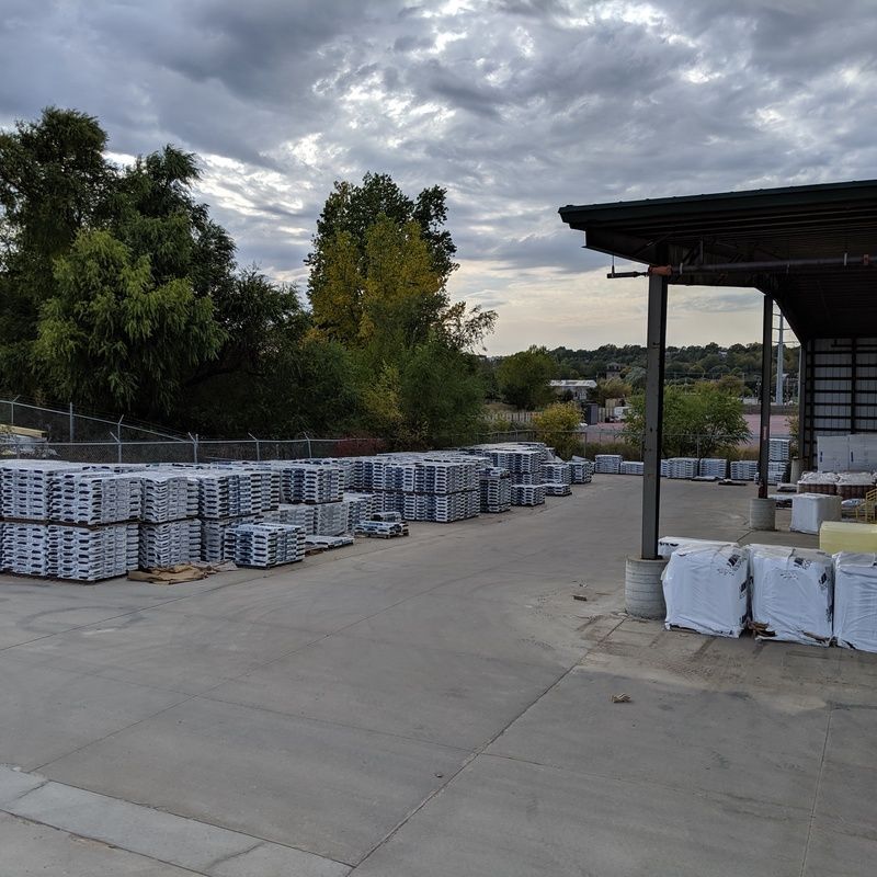Stacks of packaged construction materials sit outside a warehouse on a cloudy day.