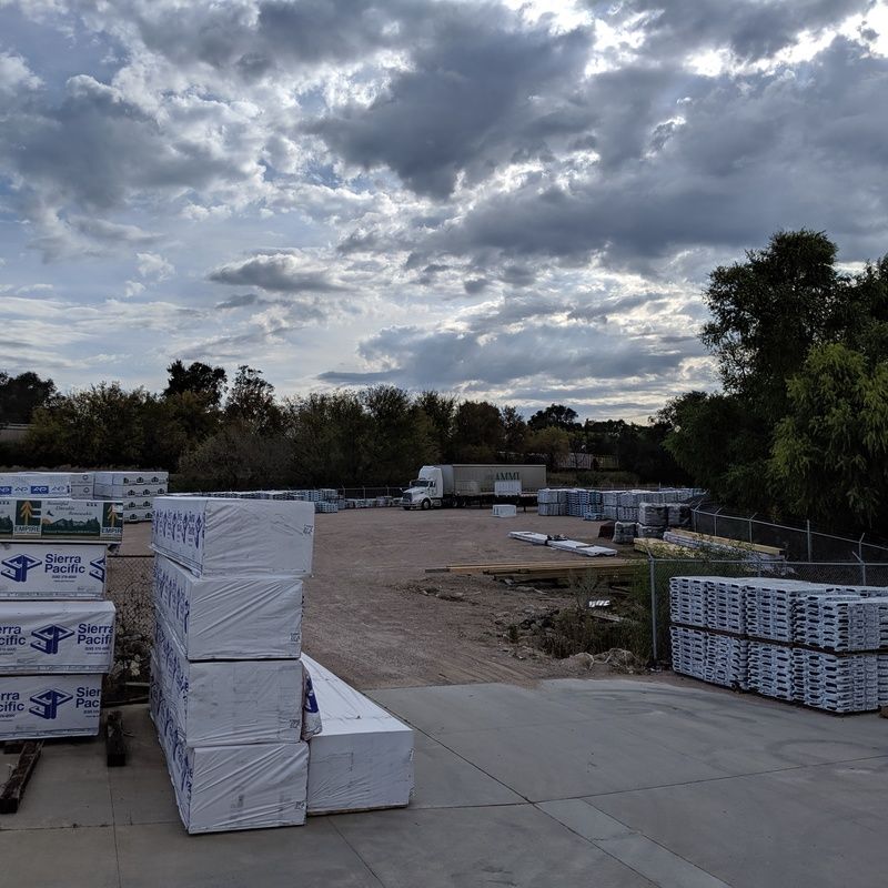 Lumberyard with stacks of wrapped lumber under a cloudy sky.