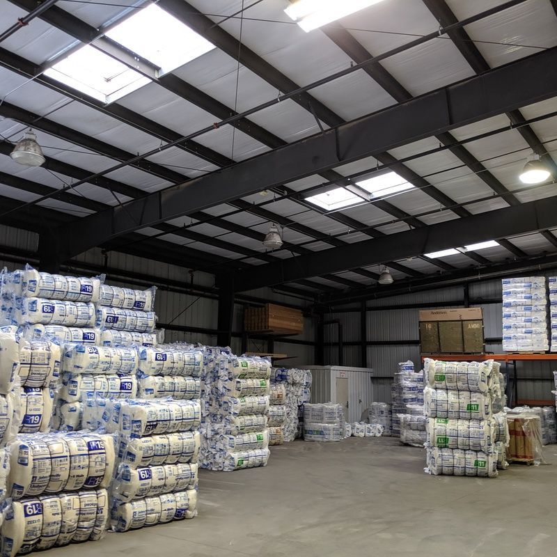 Warehouse interior with stacked bundles of white insulation. Skylights in ceiling provide daylight.