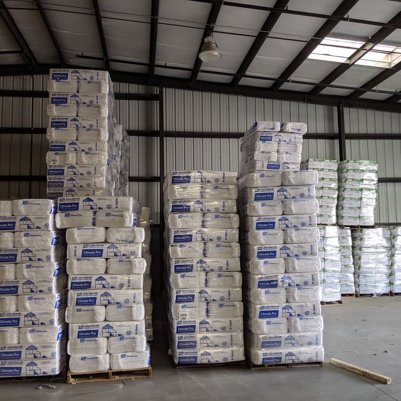 Stacks of packaged insulation stored in a metal warehouse.