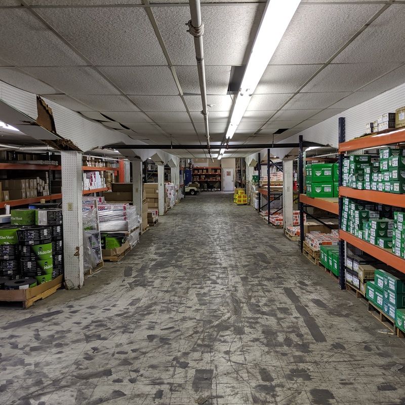 Warehouse interior with shelves of items, concrete floor, and fluorescent lights.