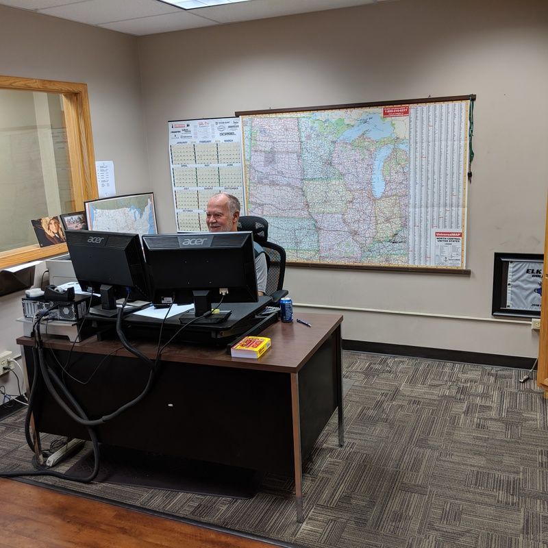 Man at desk with two monitors, map on wall, office setting.