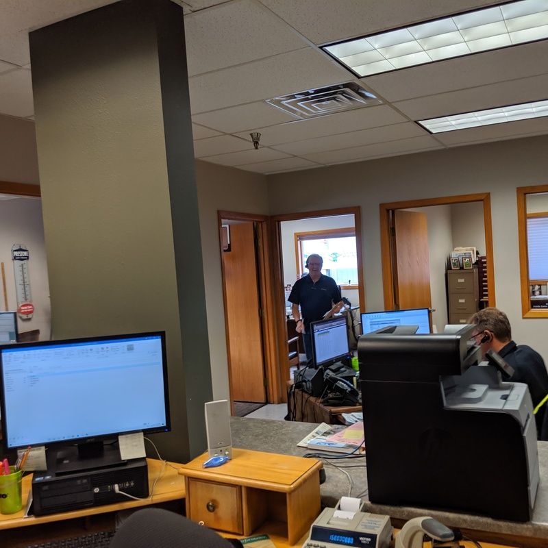 Office interior with people working at computers, one in doorway.