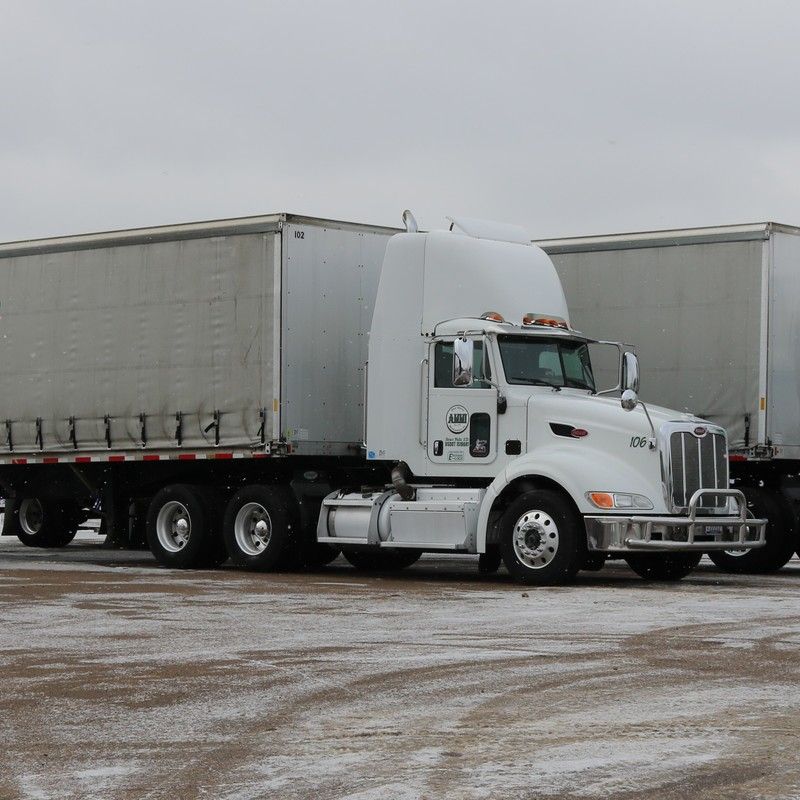 White semi-truck with a cargo trailer parked outdoors on a snowy surface.
