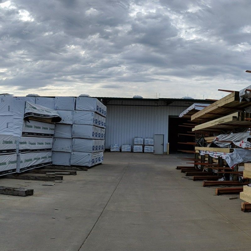 Lumberyard with stacks of packaged wood and building under a cloudy sky.