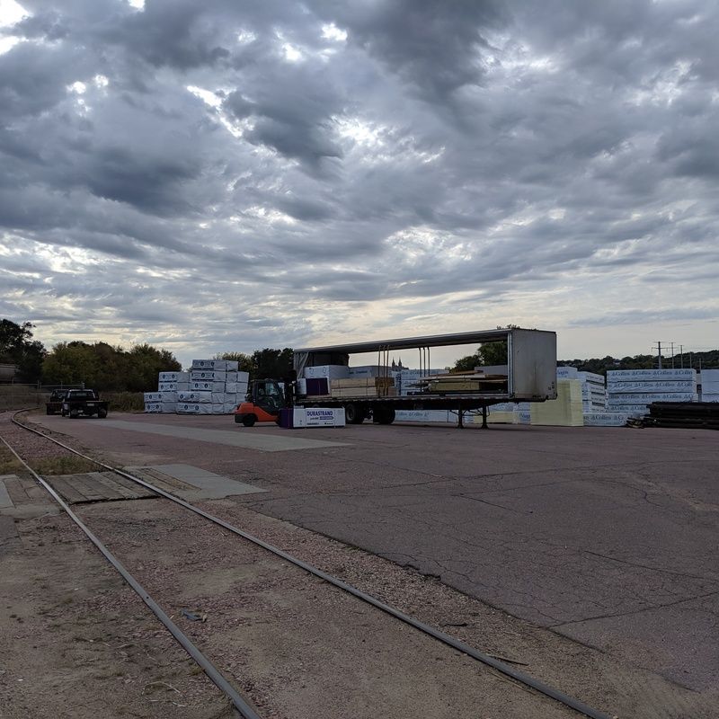 Forklift loading lumber onto a flatbed trailer at a lumberyard under a cloudy sky.
