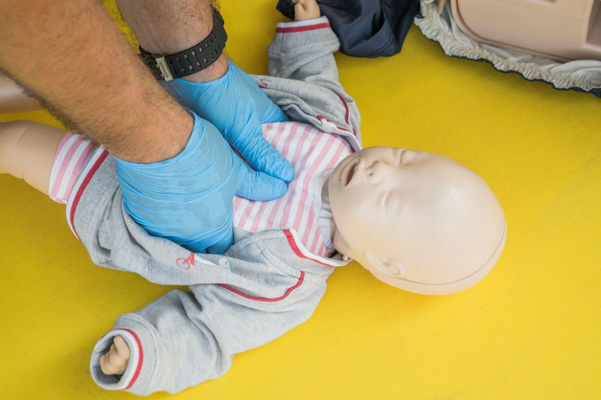 A man is giving a baby a heart massage on a yellow mat.