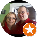 Two people smile at the camera. A woman with glasses and a man in a red shirt stand close together indoors.