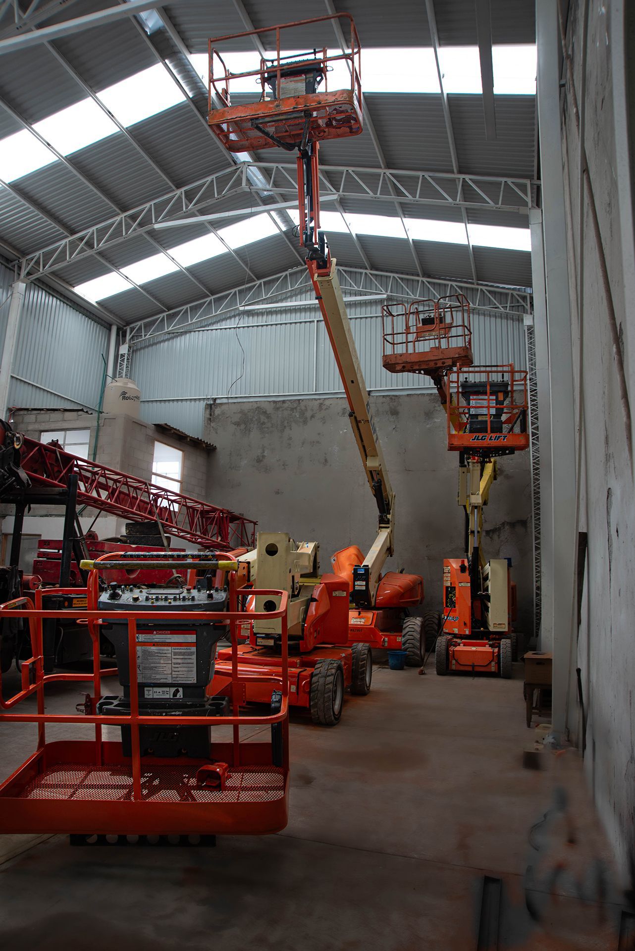 Varias plataformas elevadoras naranjas dentro de un almacén con techo metálico y paredes de hormigón.