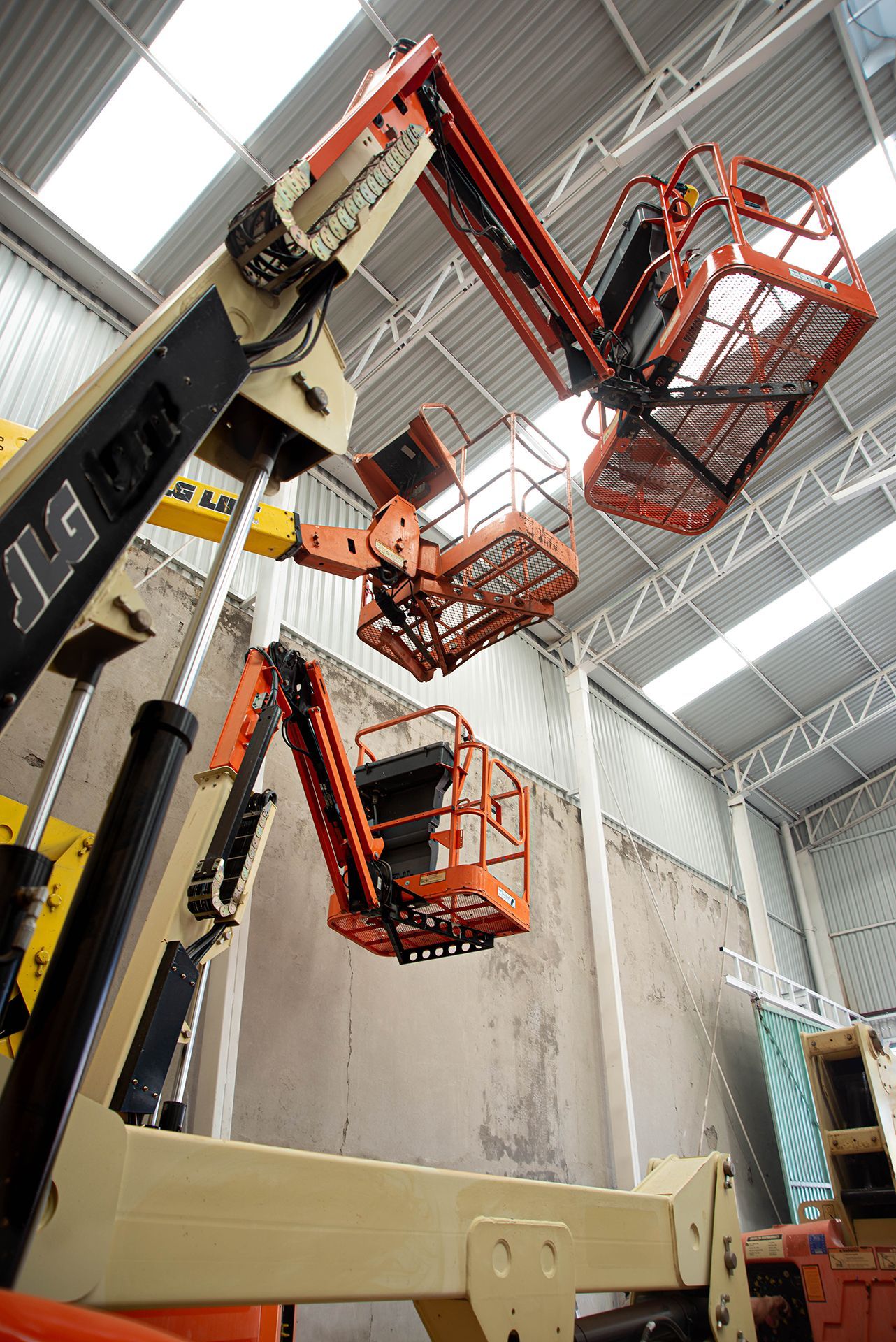 Tres plataformas elevadoras de color naranja, ubicadas en el interior de un almacén y situadas en diferentes ángulos.
