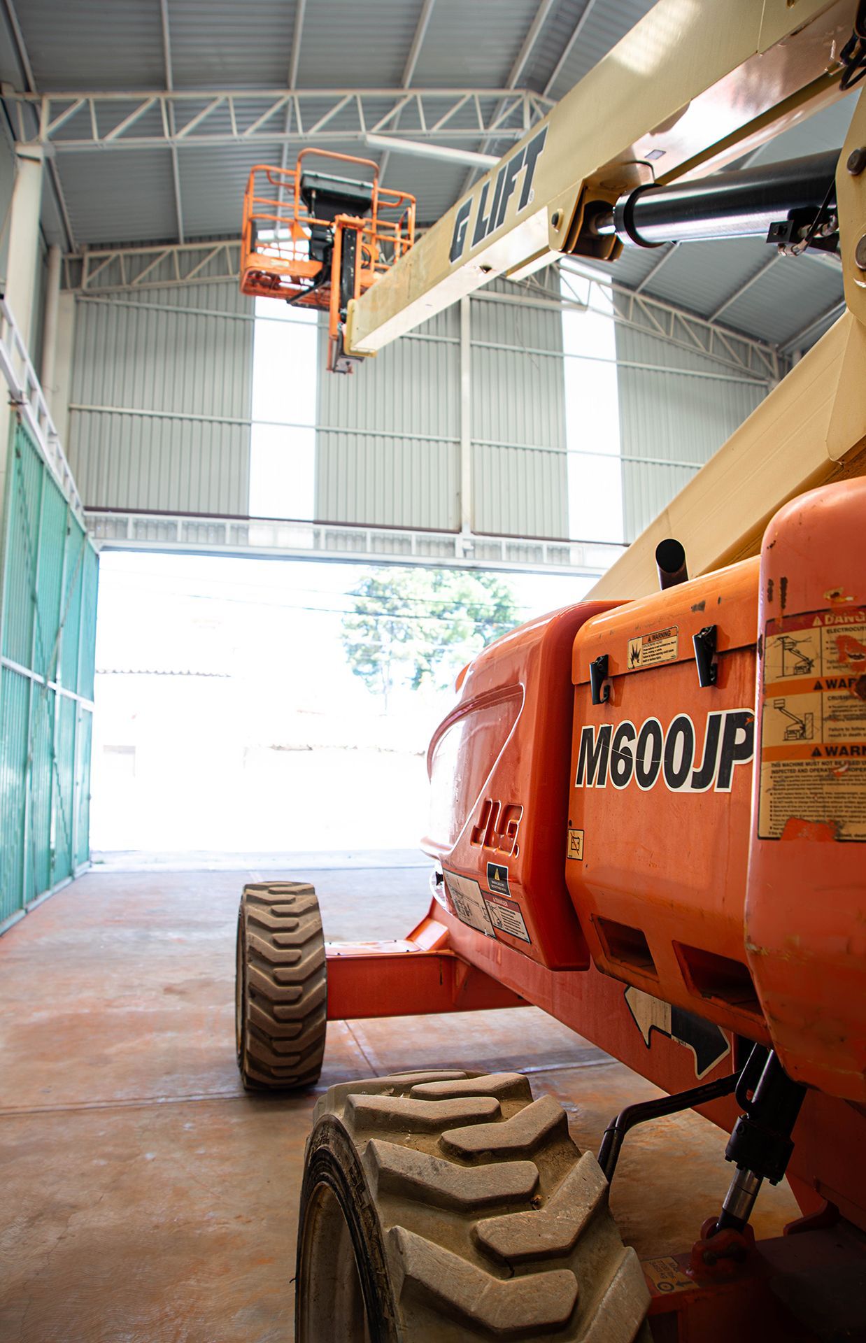 Elevador Orange JLG S600JP extendido dentro de un edificio con techo de metal, cerca de una puerta abierta.