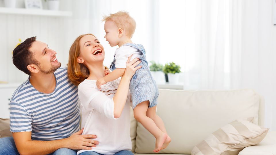 Happy young adult couple holding baby in air in clean home