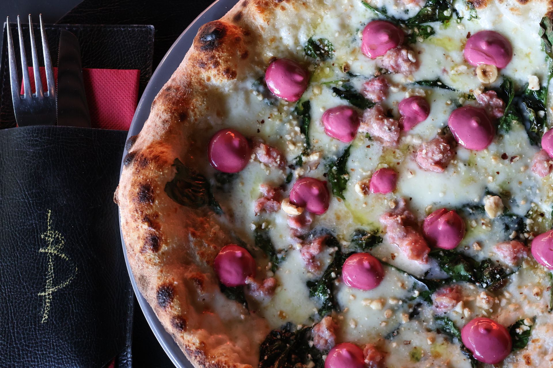 Pizza condita con cucchiaiate di salsa rosa, formaggio bianco e spinaci verdi; servita con forchetta e tovagliolo.