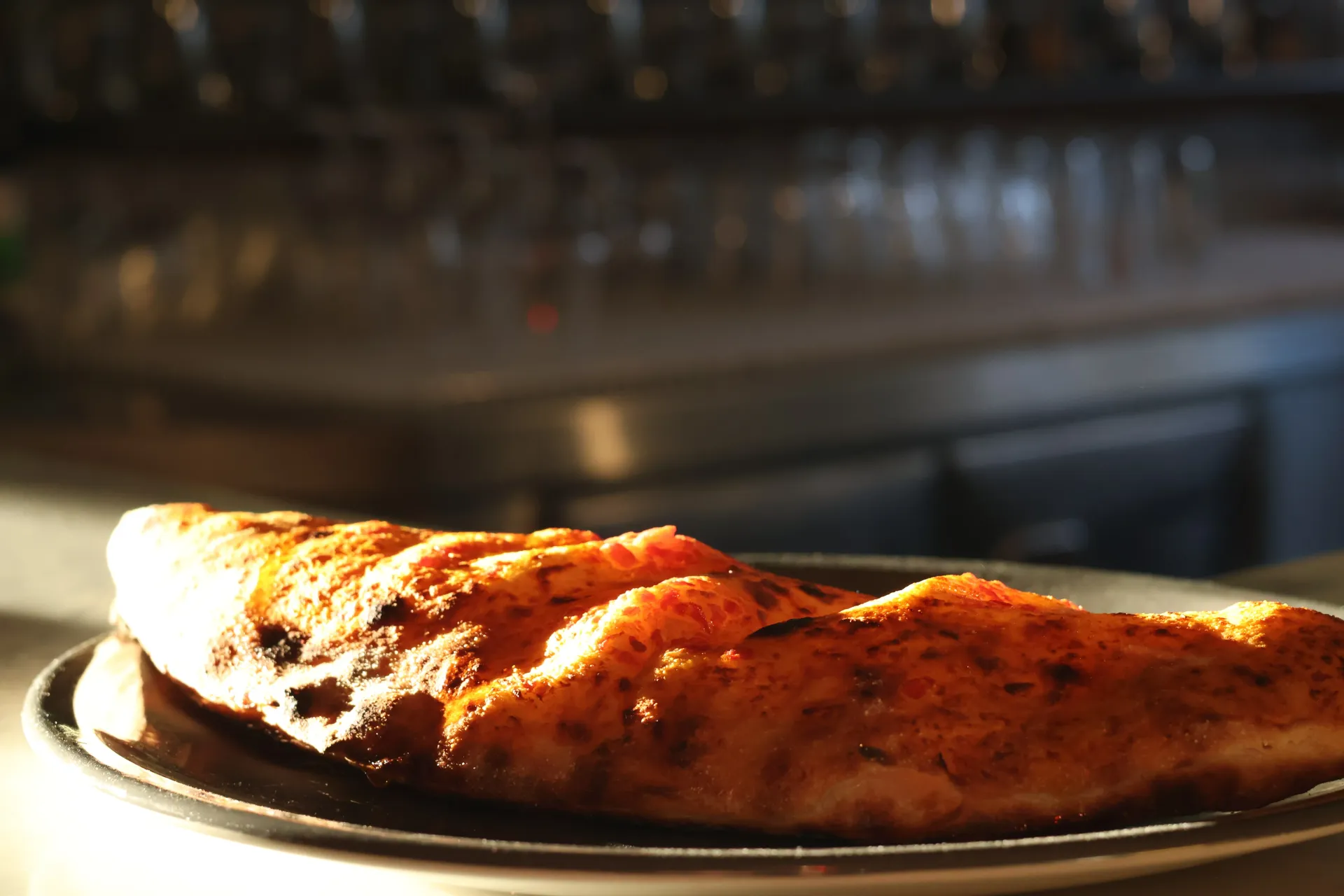 Primo piano di una crosta di pizza parzialmente mangiata e piena di bolle, su un piatto in un ristorante.