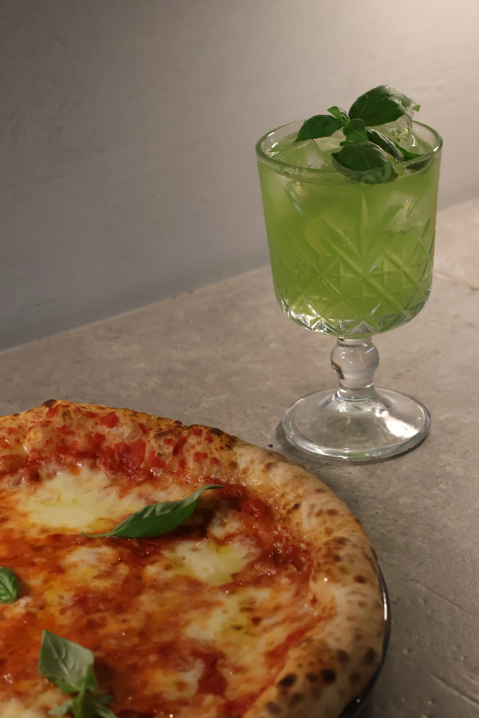 Pizza con condimento margherita e bevanda verde con ghiaccio e menta.