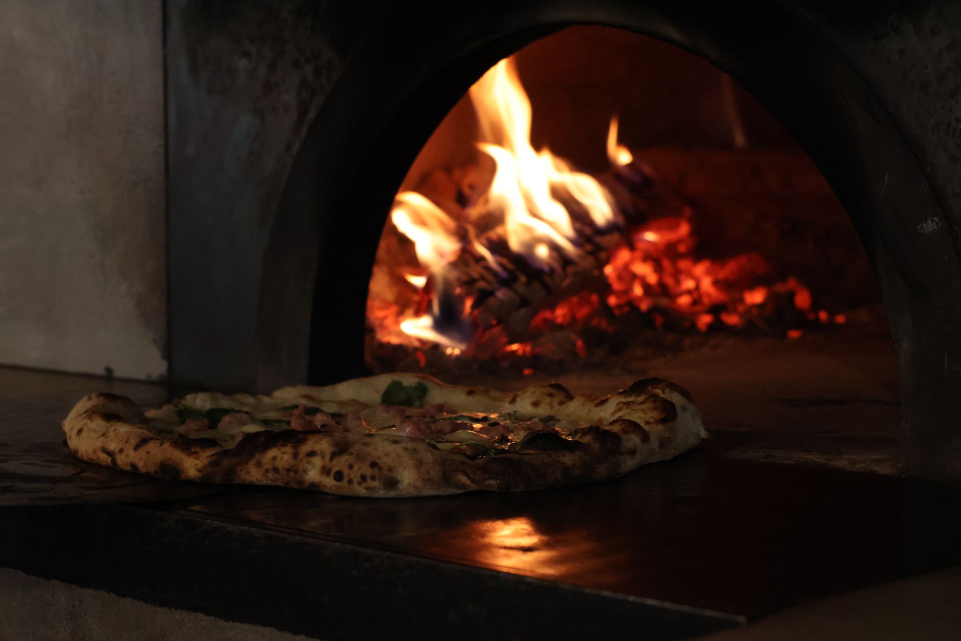 Pizza cotta nel forno a legna con fiamme sullo sfondo.