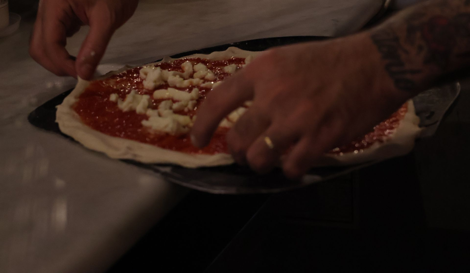 Persona che aggiunge formaggio alla pizza con salsa di pomodoro su una pala.