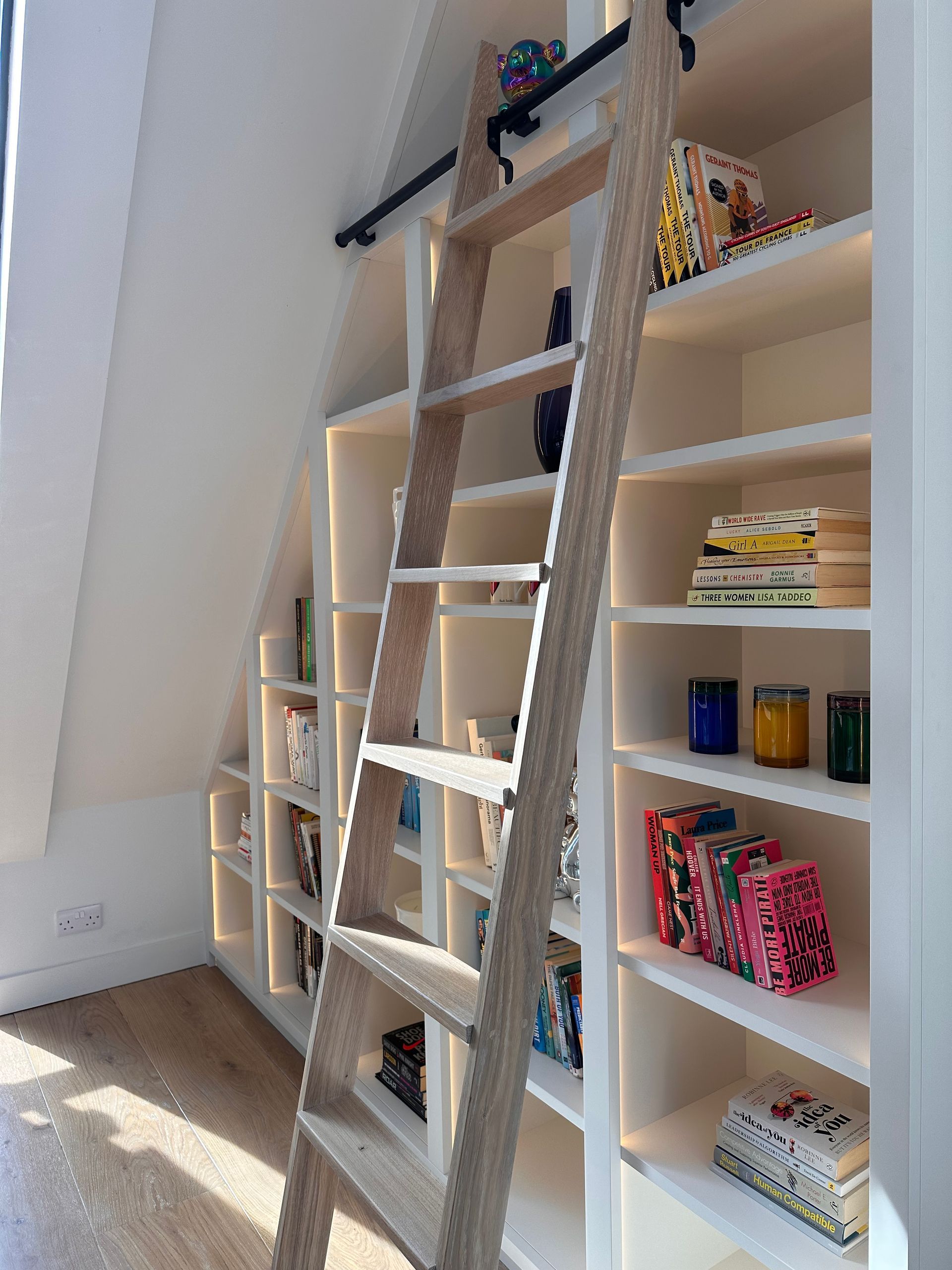 a wooden ladder is leading up to a bespoke library furniture filled with books .
