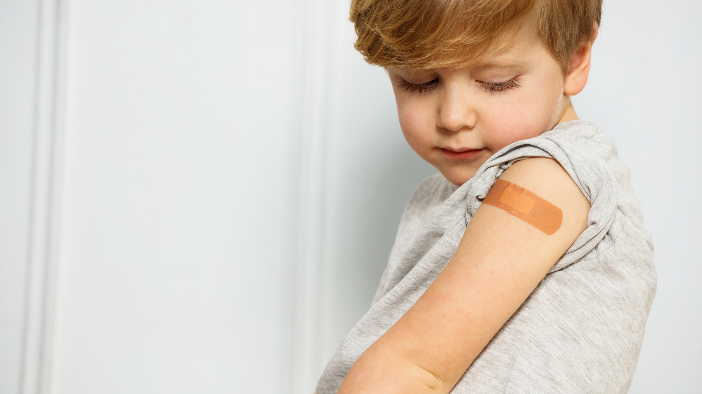 Child looking down with an adhesive bandage on the upper arm against a light background