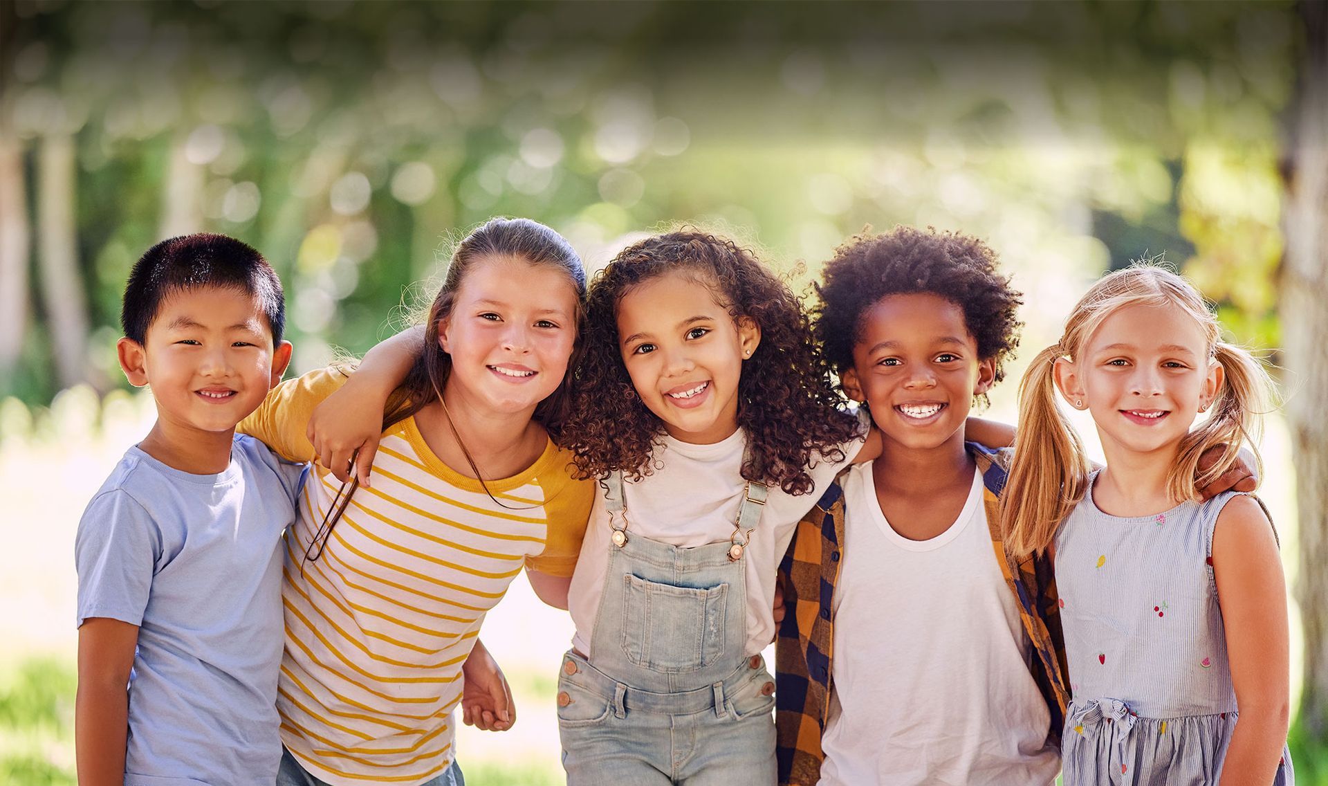 Five smiling children standing arm in arm outdoors