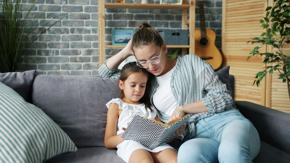 Adult and child reading a book together on a gray couch in a cozy living room
