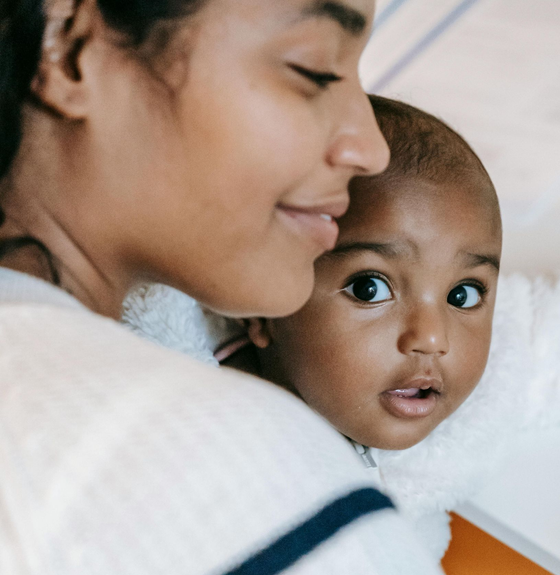 Close-up of a woman holding a wide-eyed baby, both in soft white clothing.