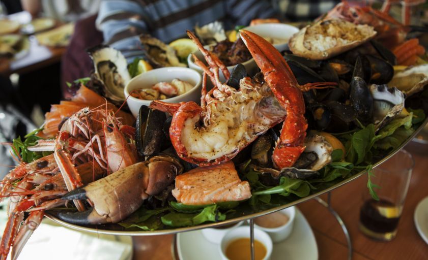 Food near to our properties to buy or rent in the Cayman Islands. Seafood platter: lobster, crab, shrimp, oysters, mussels, and salmon on a tiered tray, greens, sauces.