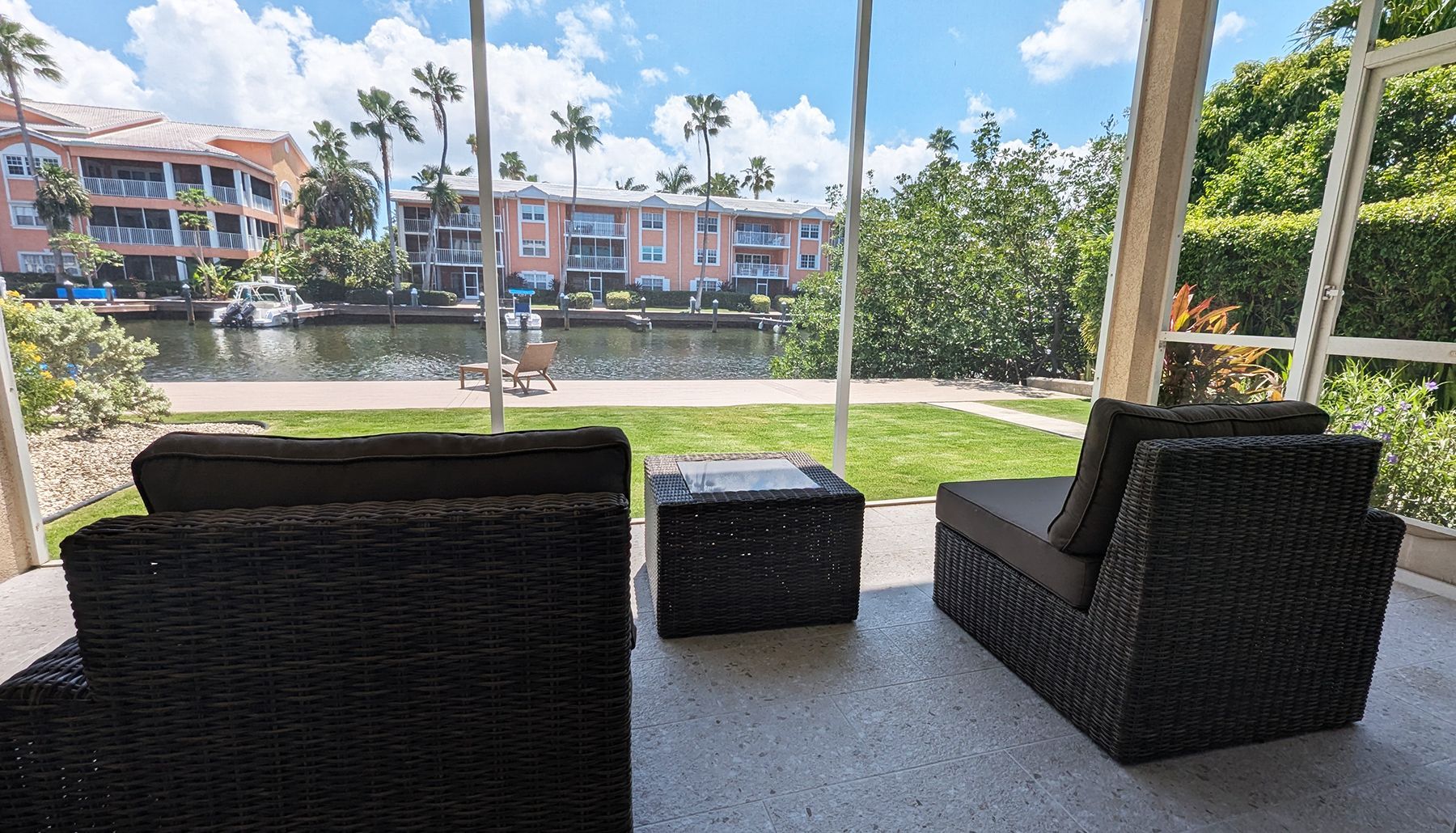 One of our properties. Patio with black wicker furniture overlooking a waterway with buildings and palm trees.