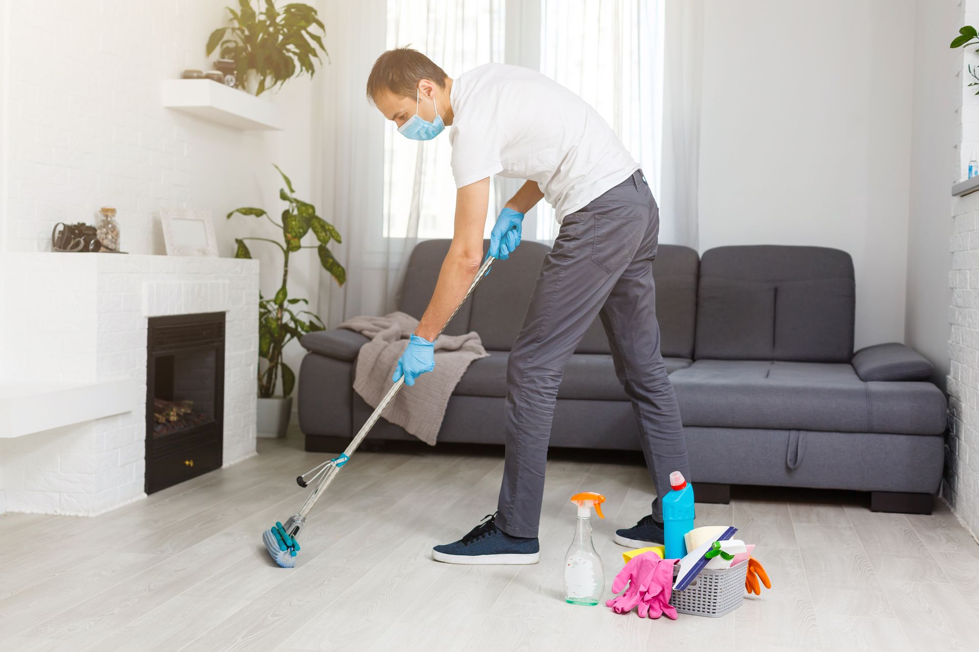 A man wearing a mask and gloves is cleaning the floor in a living room.