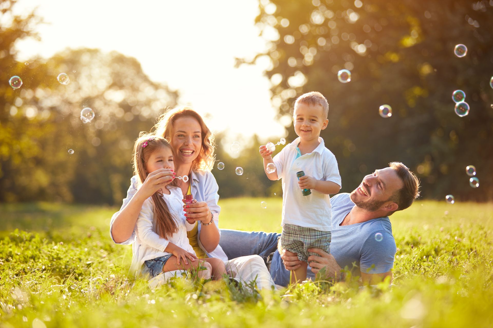 A family is sitting in the grass blowing soap bubbles.