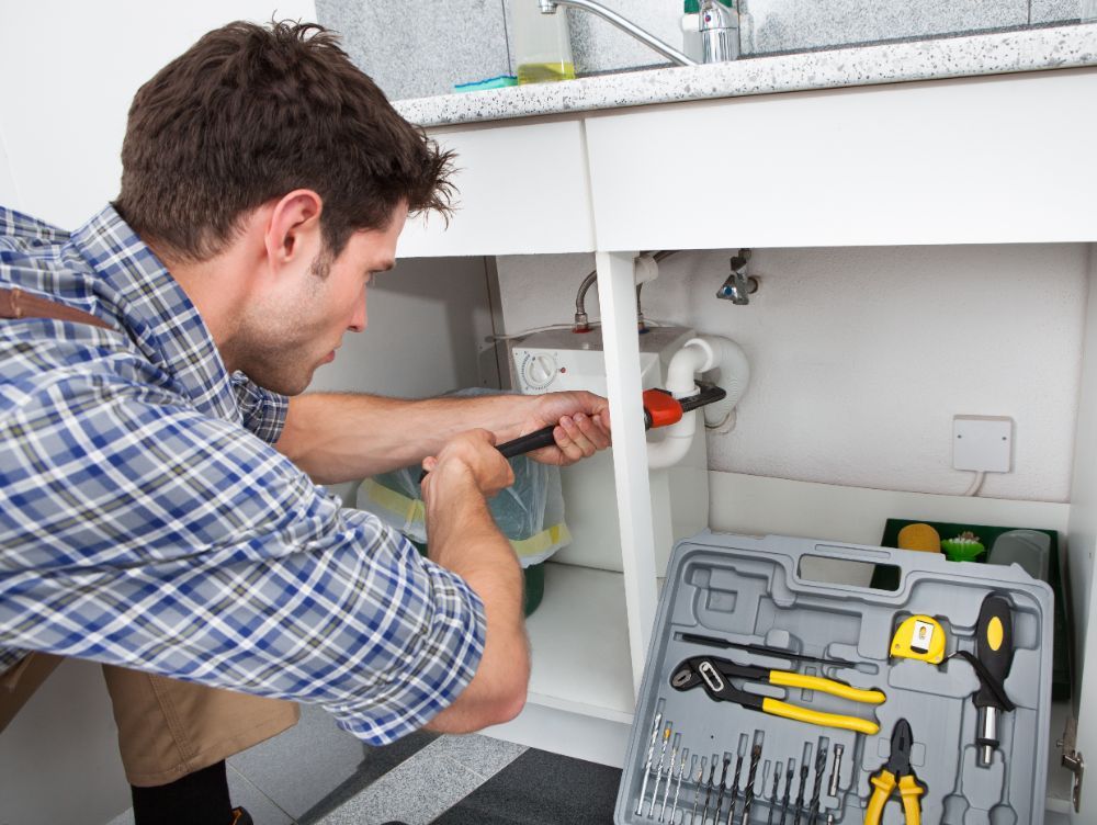 an expert fixing the pipes underneath a kitchen sink