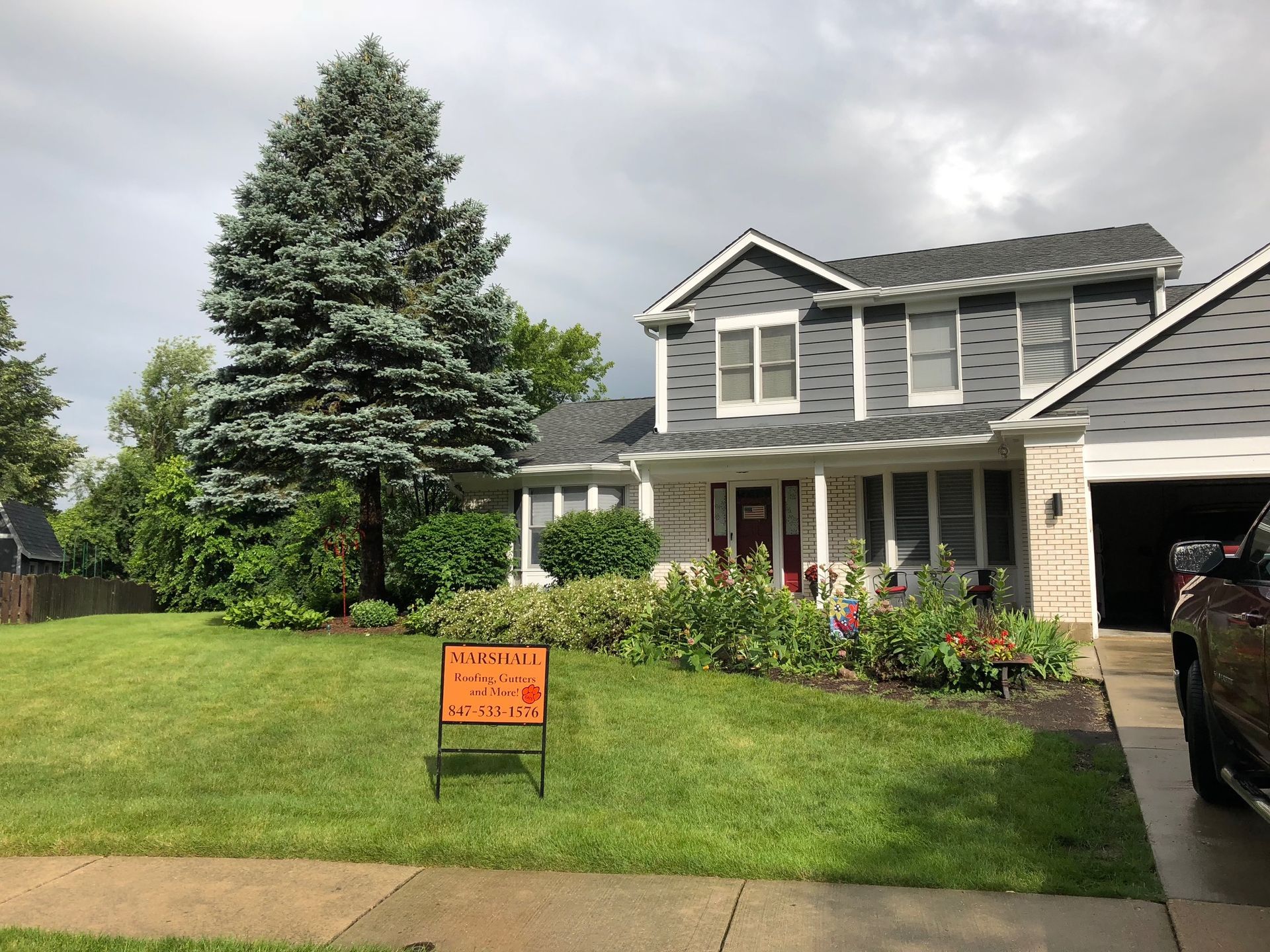 A car is parked in front of a house with a sign in front of it.