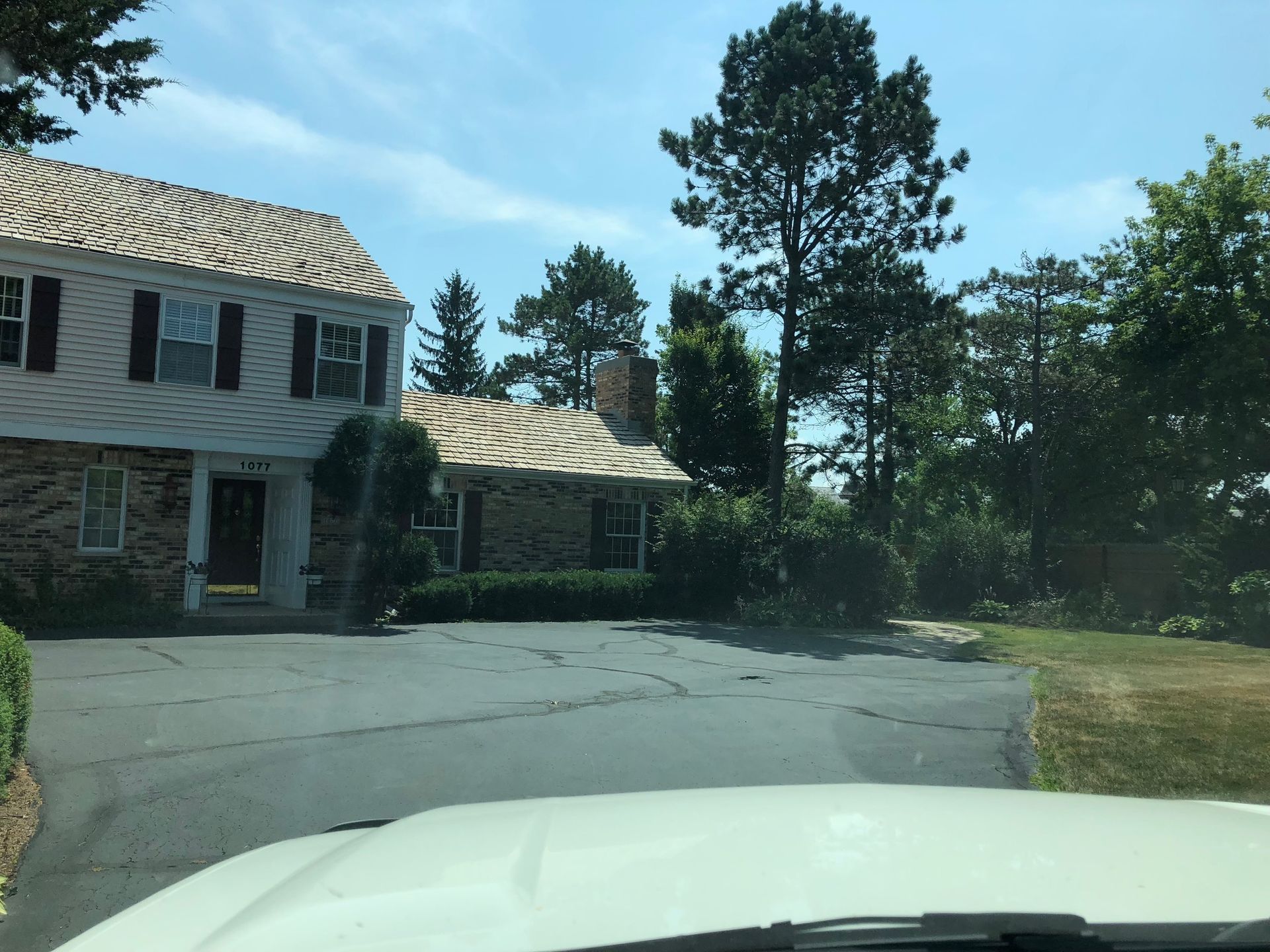 A white car is parked in front of a large house