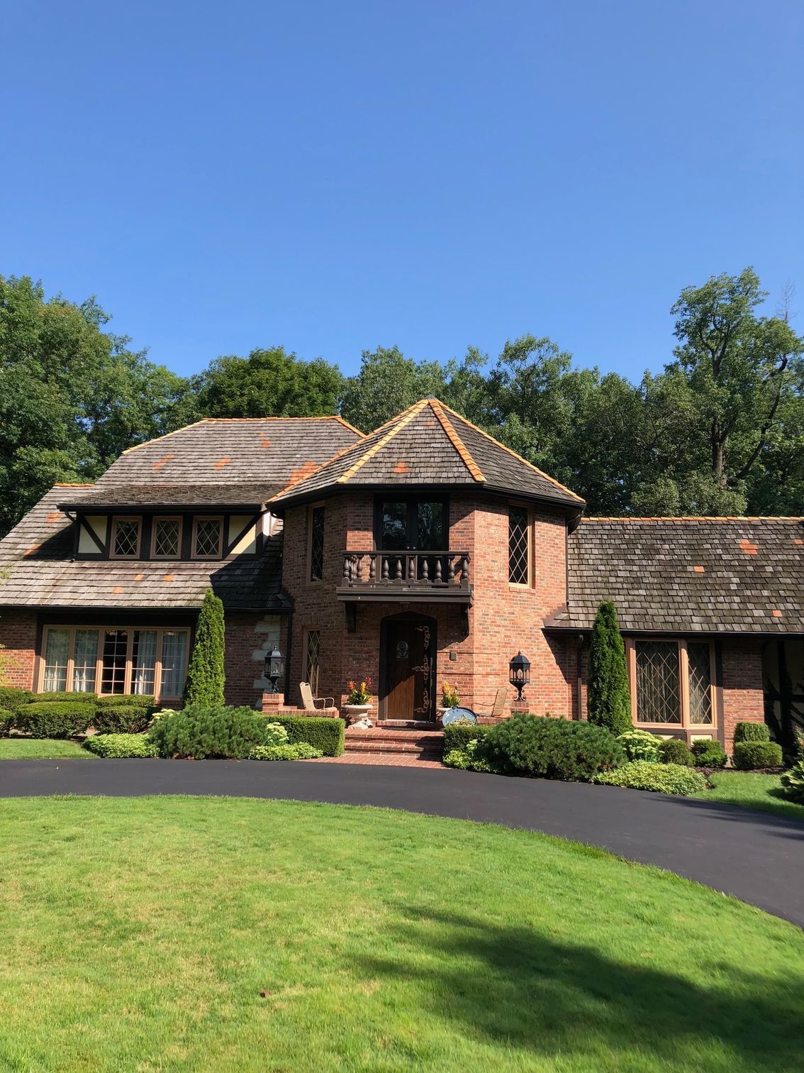 A large brick house with a wooden roof is surrounded by trees and grass.