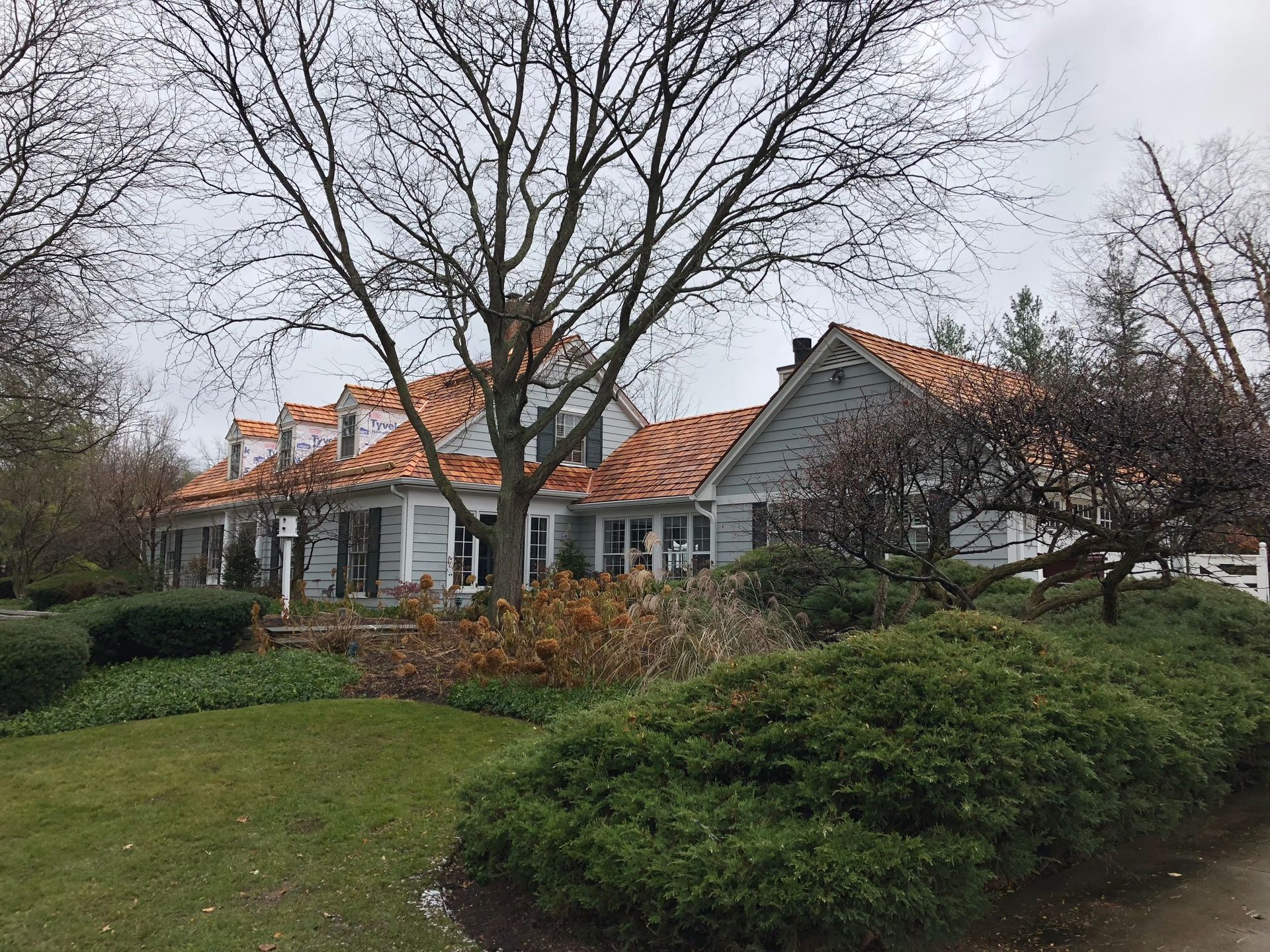 A large white house with a red tile roof is surrounded by trees and bushes.