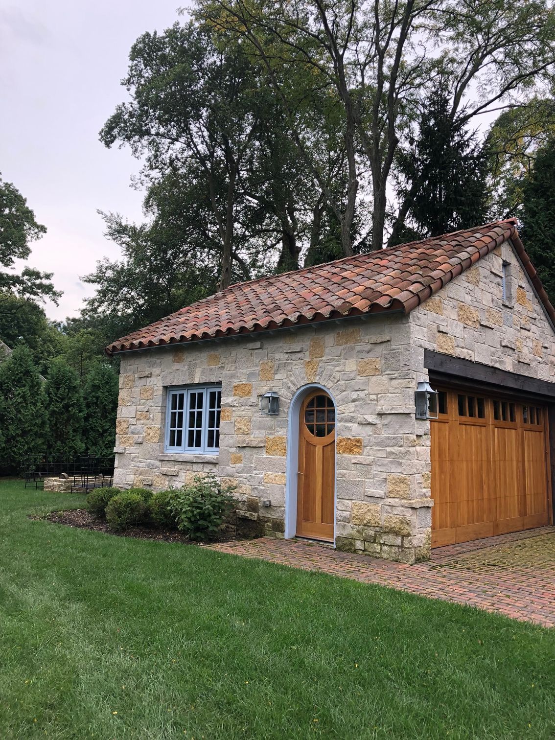 A small stone house with a wooden garage door and a tiled roof.