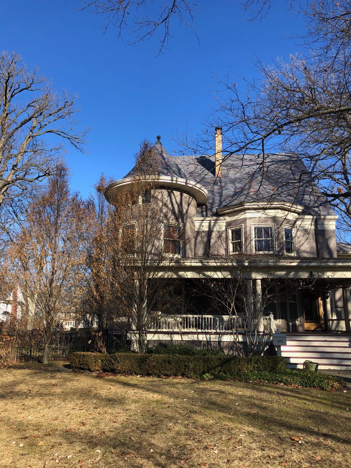 A large house with a large porch is surrounded by trees on a sunny day.