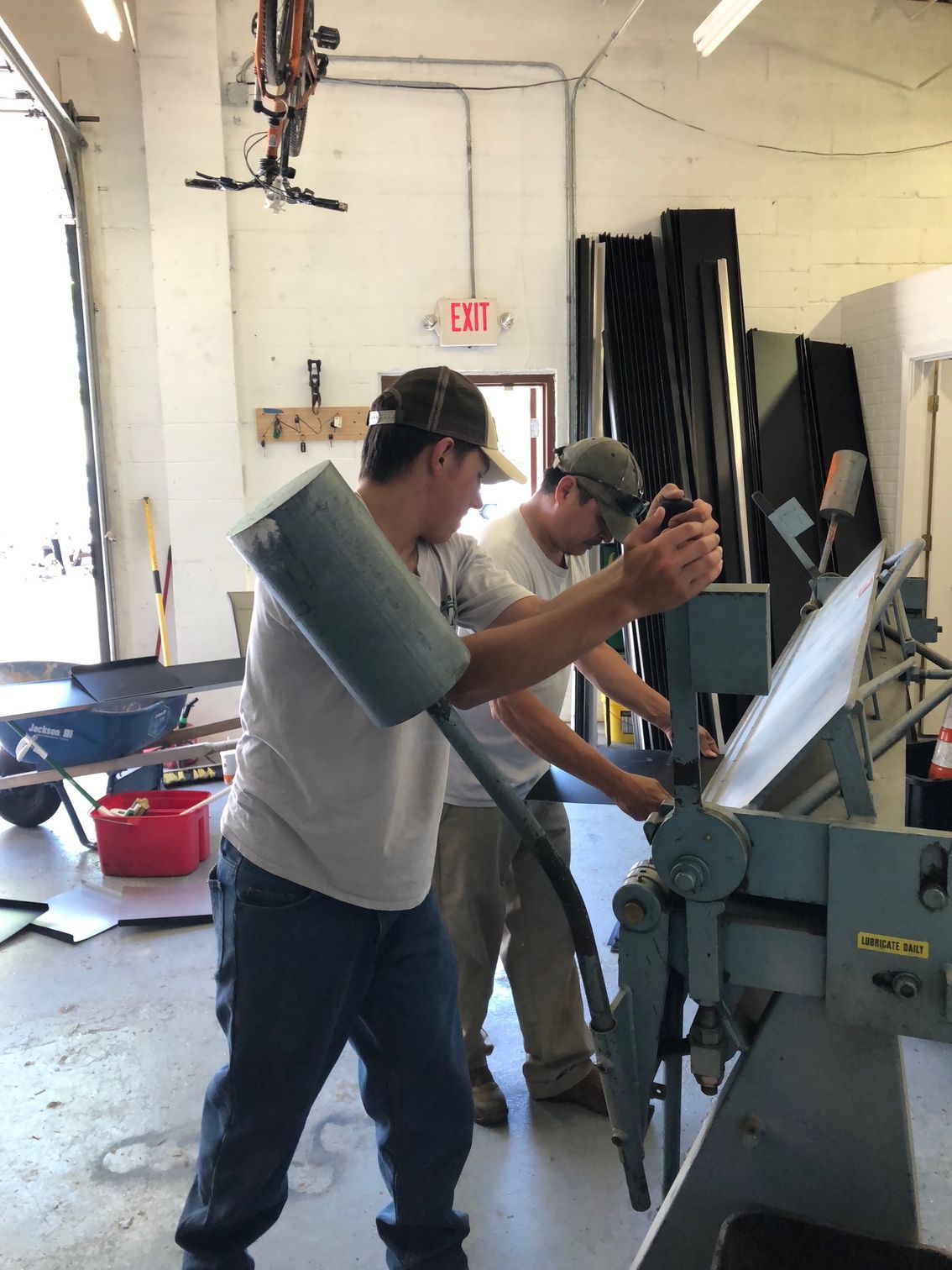 Two men are working on a machine with an exit sign in the background