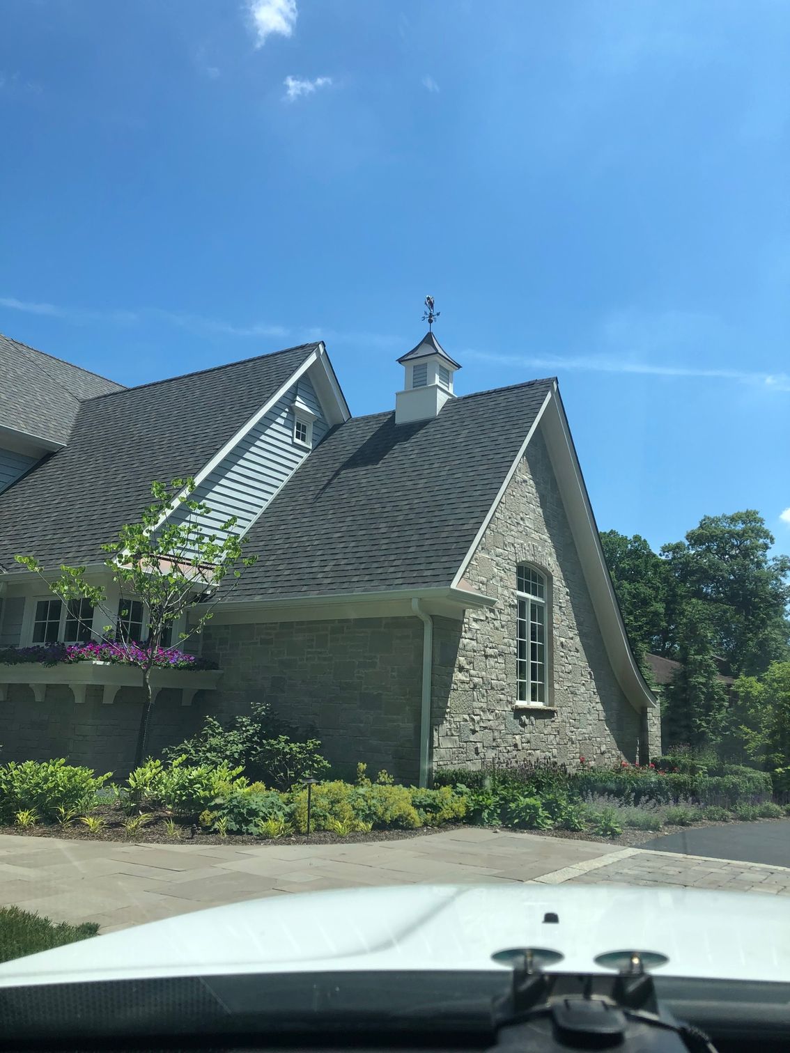 A white car is parked in front of a large house with a steeple on the roof.