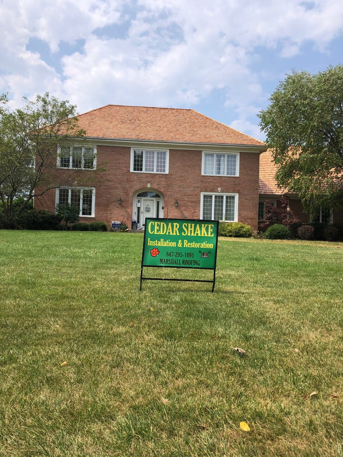 A large brick house with a for sale sign in front of it.