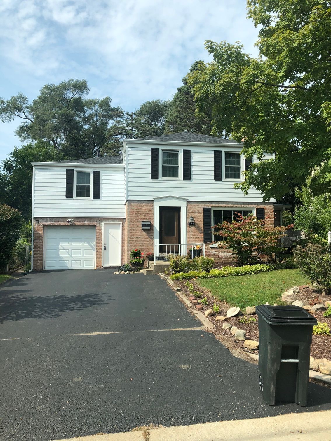 A white house with a black garbage can in front of it