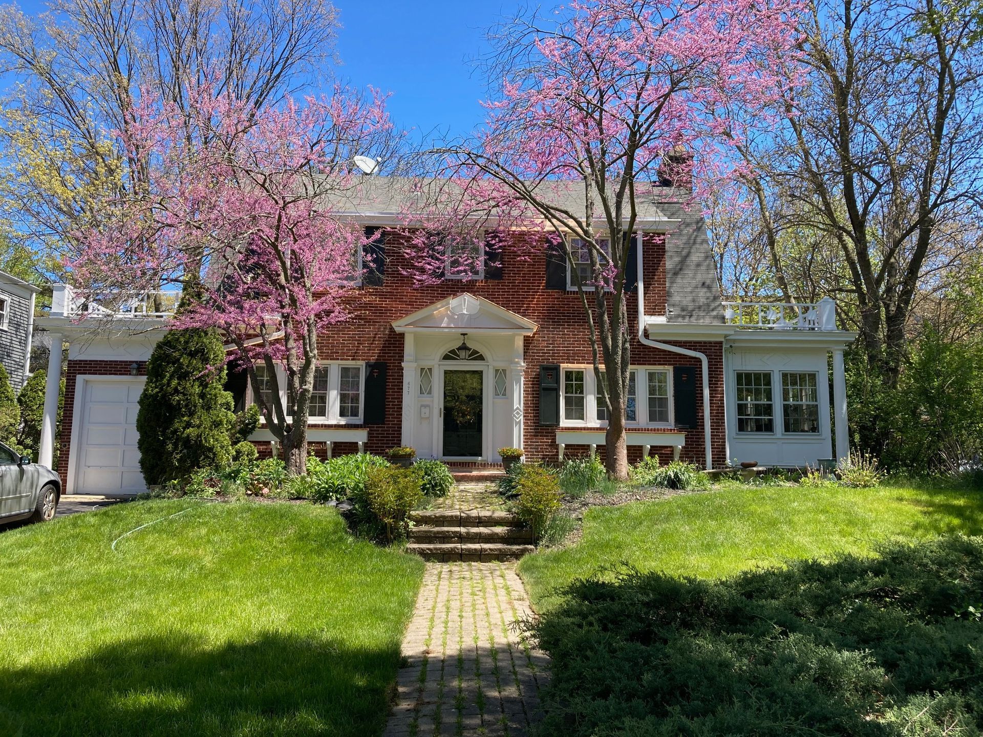 A large red brick house with pink flowers in the front yard.