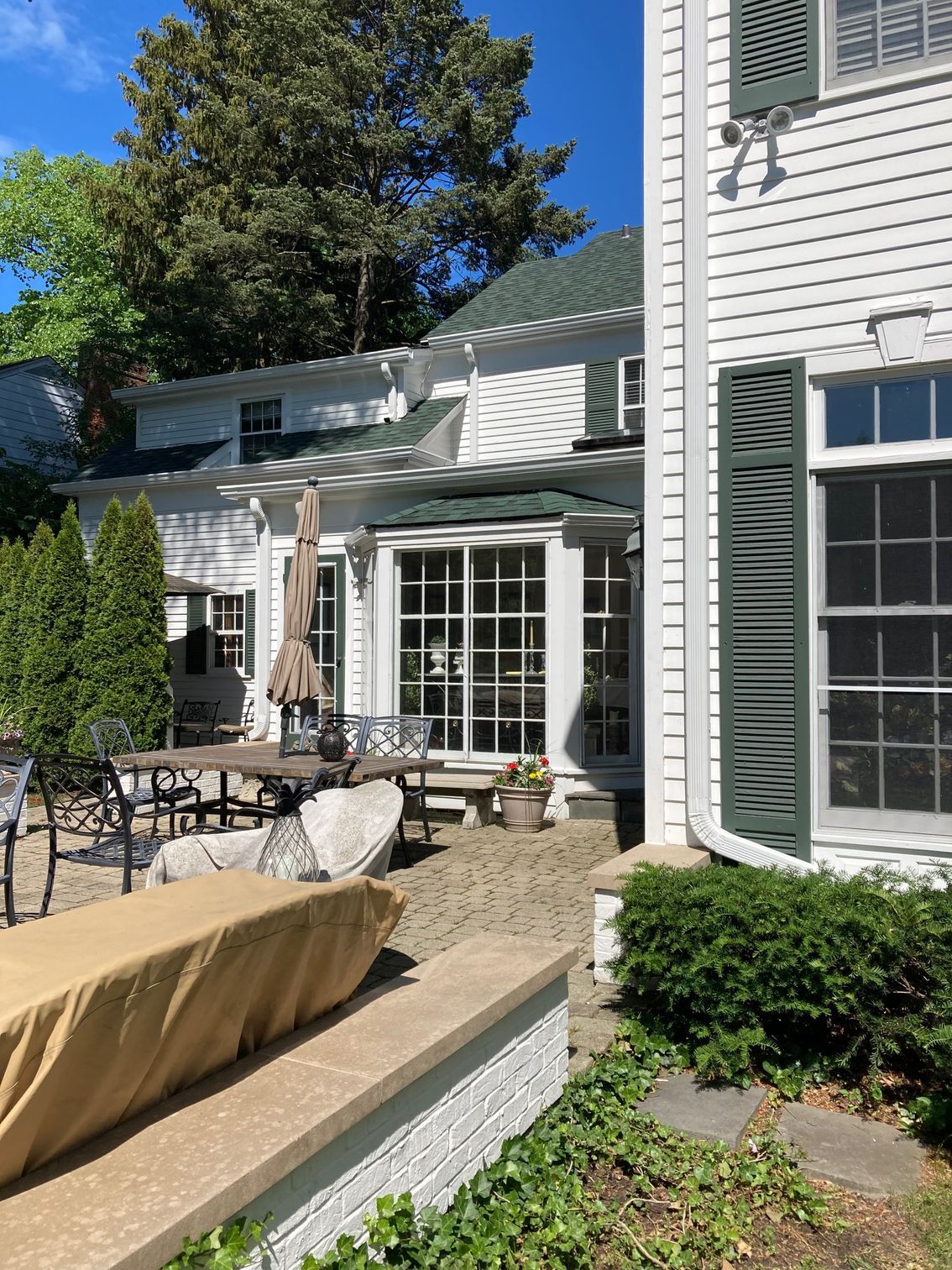 A white house with green shutters and a patio with a table and chairs.