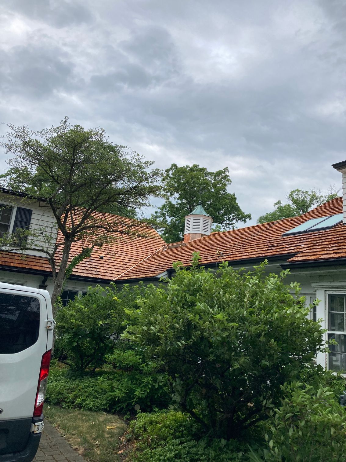 A white van is parked in front of a house with a tiled roof.