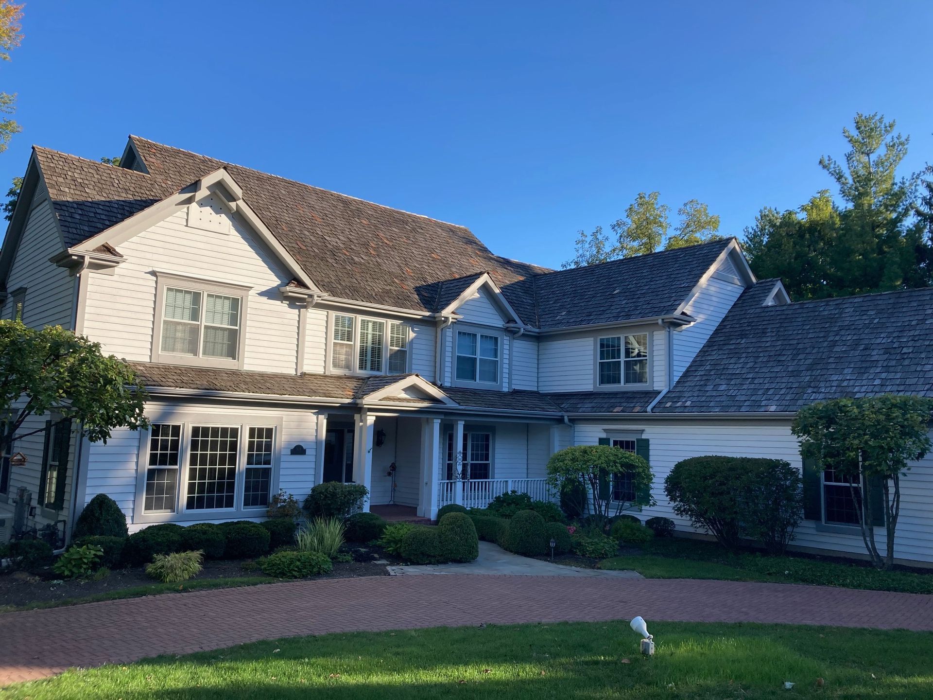 A large white house with a gray roof is sitting on top of a lush green lawn.